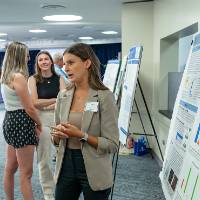 Scholar giving poster presentation to mentor.